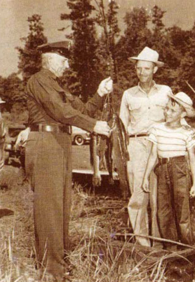 黑白照片中，一名狩猎监督员手拿鱼，与两个人交谈