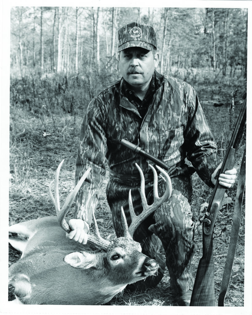 一张黑白照片,照片上有一名男子、一只鹿和一支前膛枪