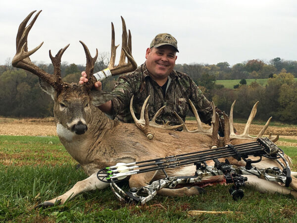 一名猎人站在他用弓箭射杀的公鹿旁边
