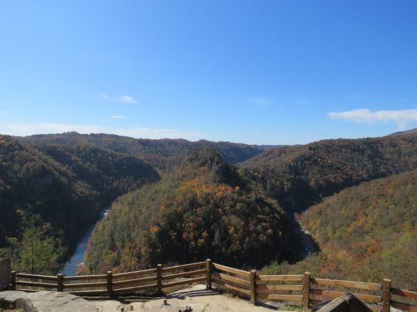 这是布雷克州际公园的观景台图片，上面有美丽的秋季山脉，左下角有一条河流流淌，前景中岩石顶部有木栅栏屏障。