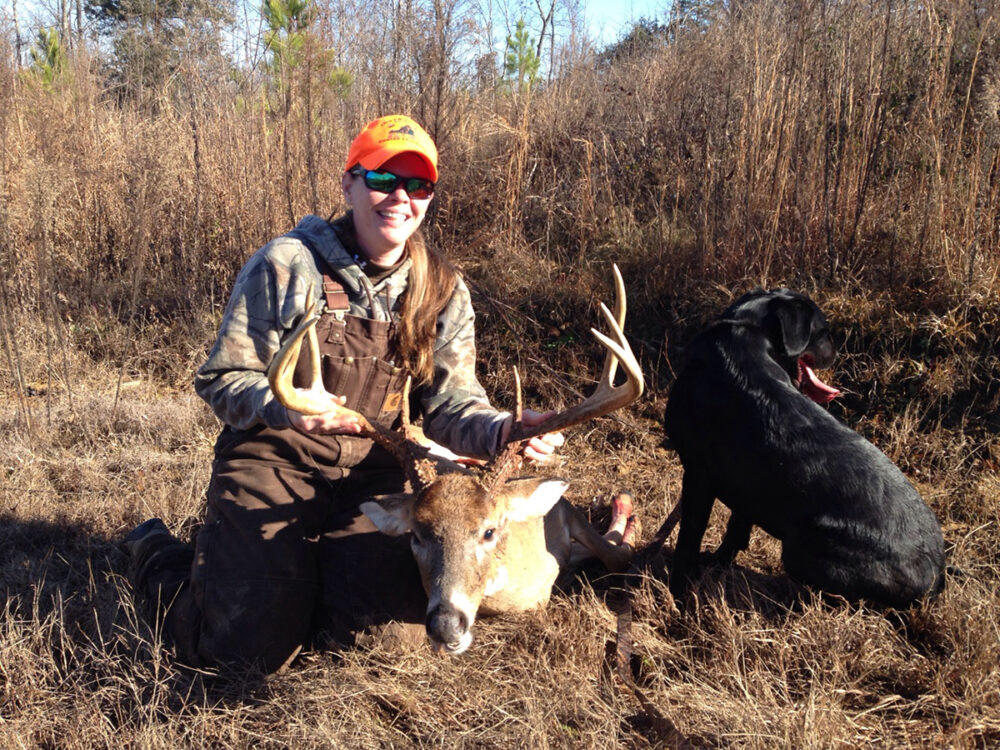 杰西卡·惠利警官和她射杀的一只鹿在她的黑色拉布拉多犬旁边合影