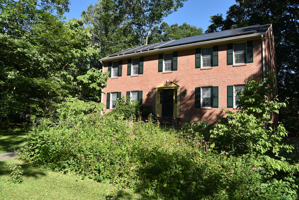 一栋砖房的图片,屋顶上装有太阳能电池板,前院有一个传粉昆虫花园