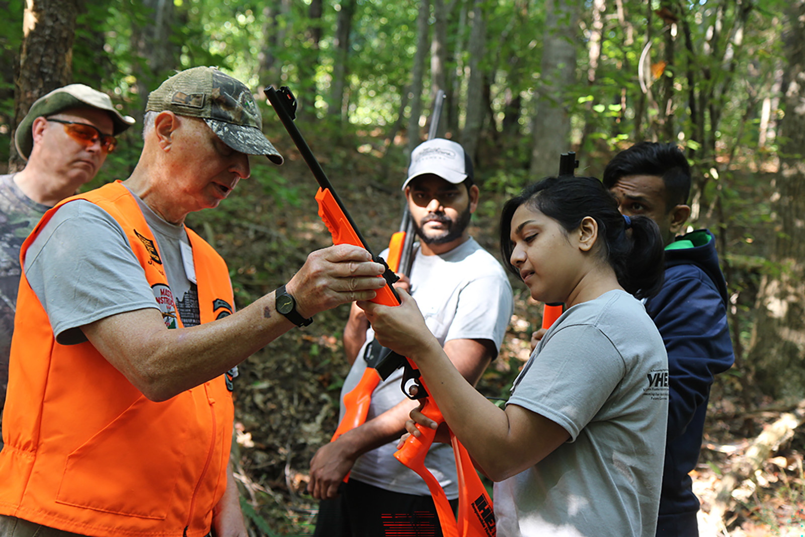 一名男子在向一名妇女讲解如何拿猎枪，一群人在一旁观看的照片。