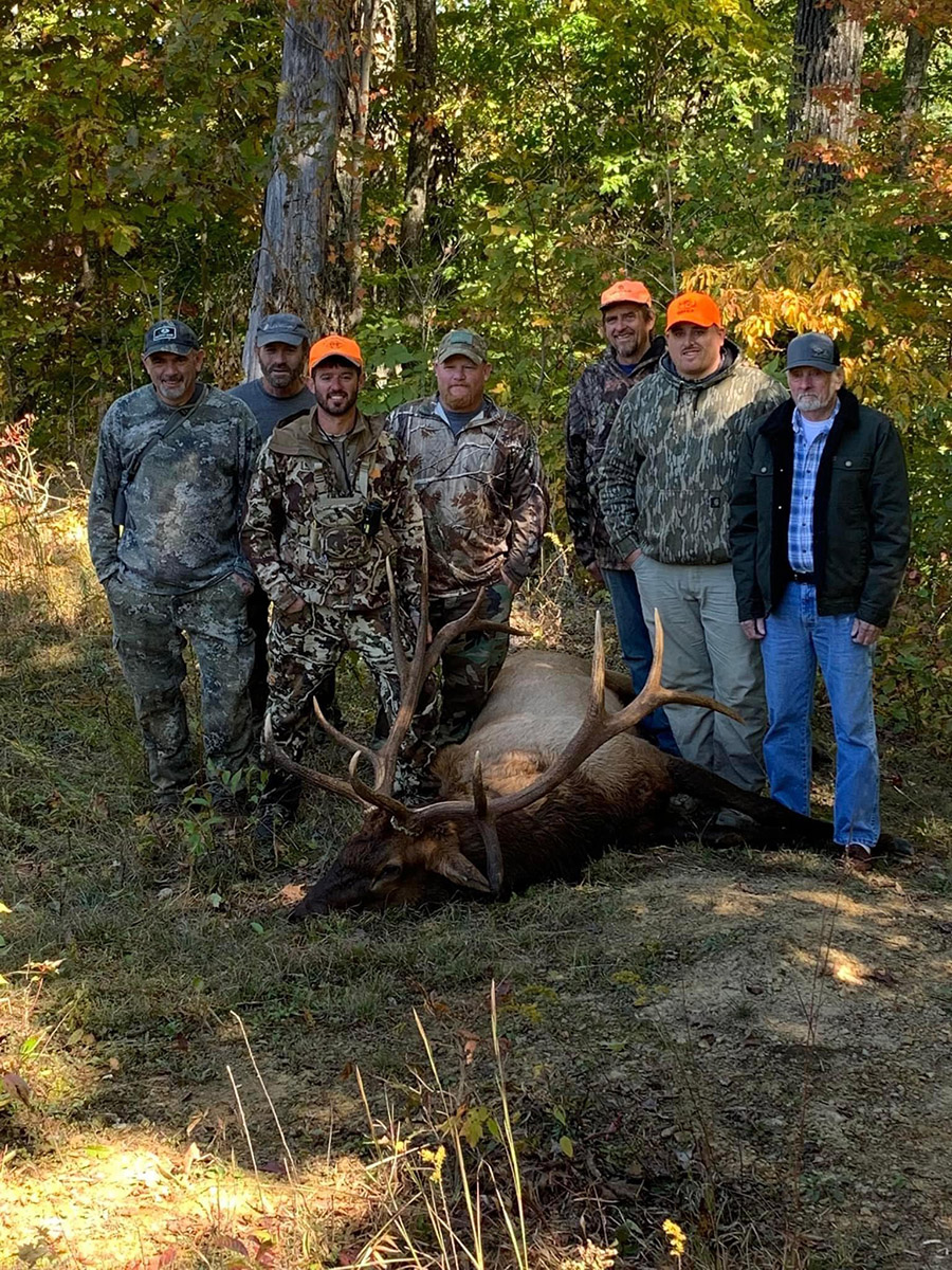 七名男子站在他们捕获的公麋鹿旁边