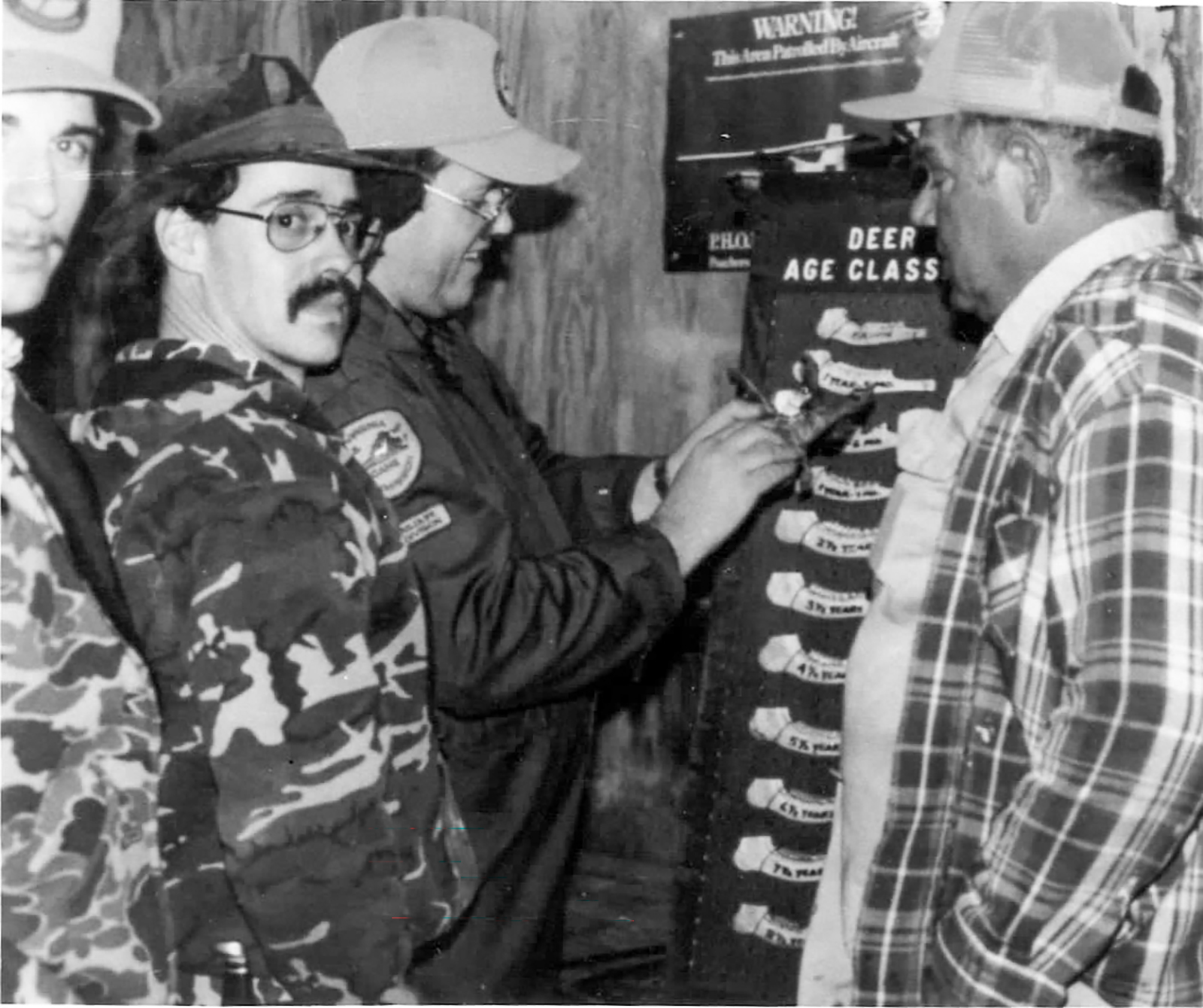 一幅黑白老照片，显示猎人正在测量鹿的颚骨。