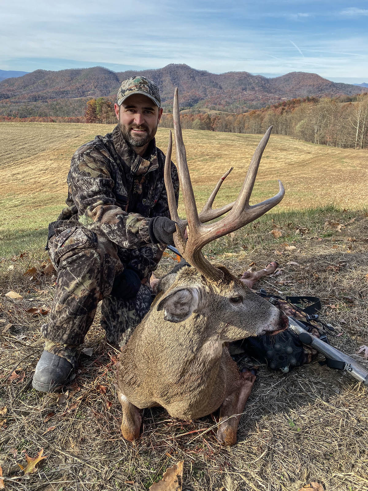 一名身着迷彩服的猎人与一只长着大鹿角的白尾鹿合影。