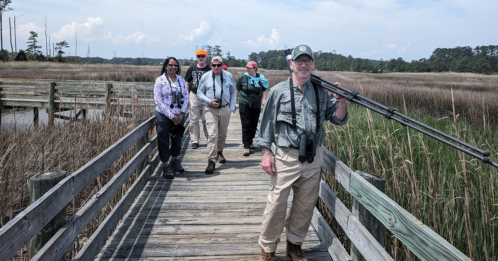五人带着双筒望远镜走在穿过湿地的木板路上的照片。