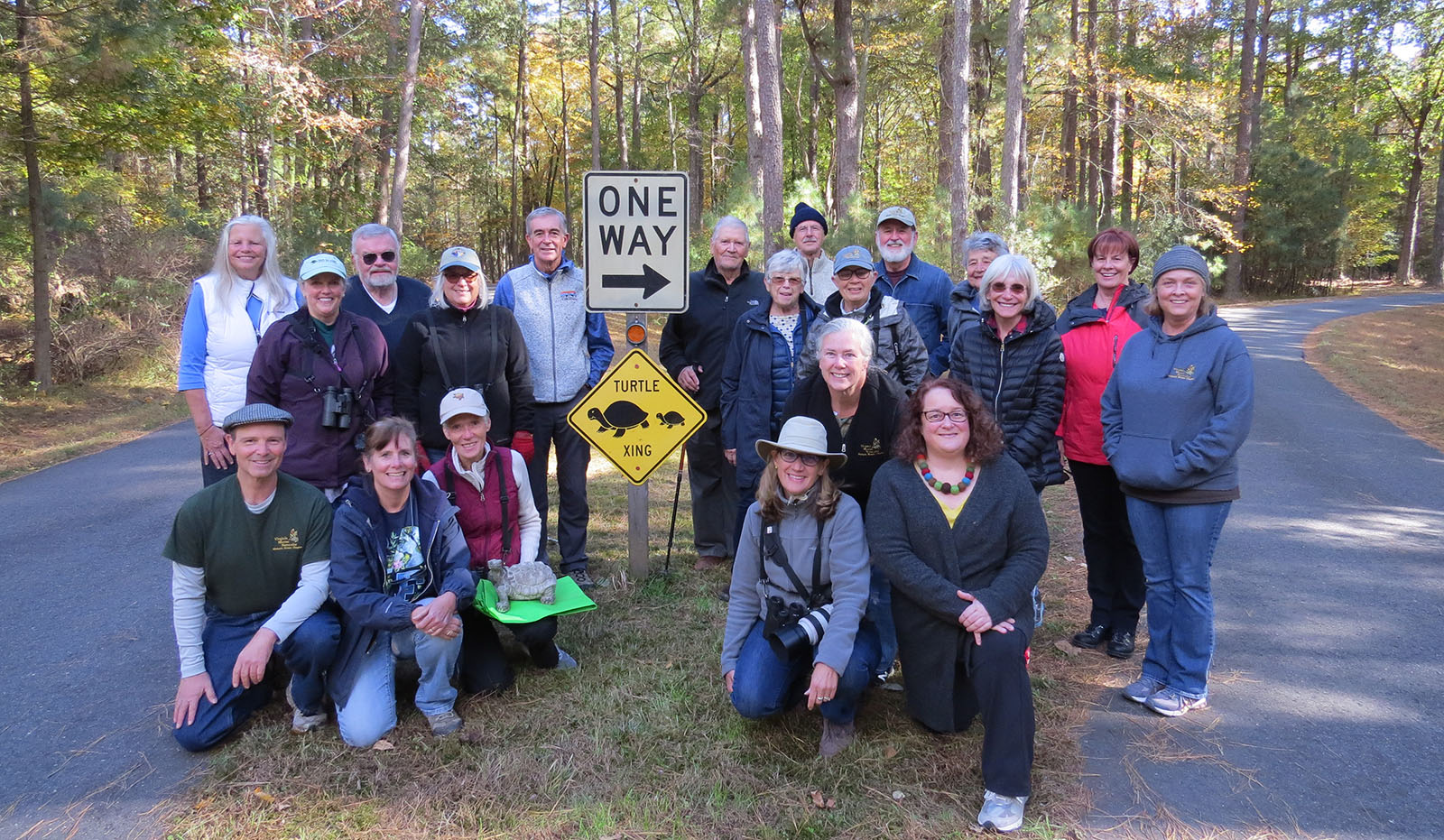一群20人聚集在一条小铺路中间的乌龟过街标志周围，一个人跪在最前面，手里拿着一座乌龟雕像。