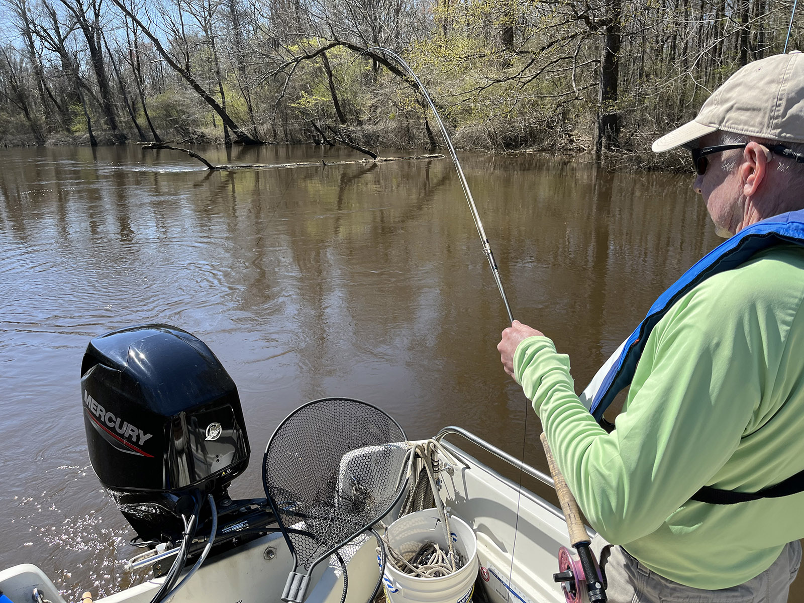 照片中，一名男子站在船上，手握飞钓竿，弯腰垂钓在水面上。