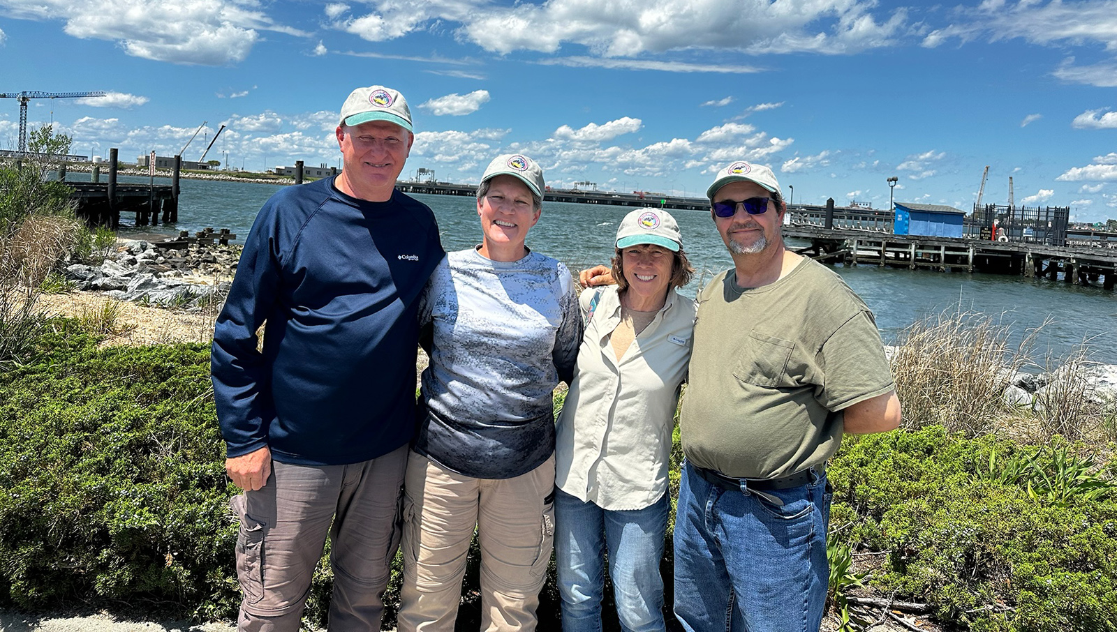 一张四个微笑的人站在岛屿海滩上的照片，背景是水。