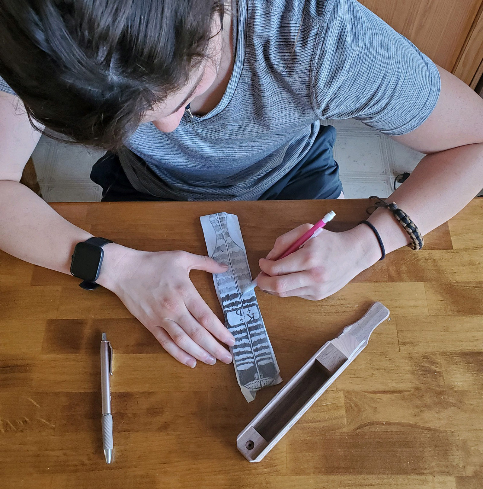 照片中，一名女孩坐在旁边的桌子上，用桨式火鸡叫器在纸上描绘图案。