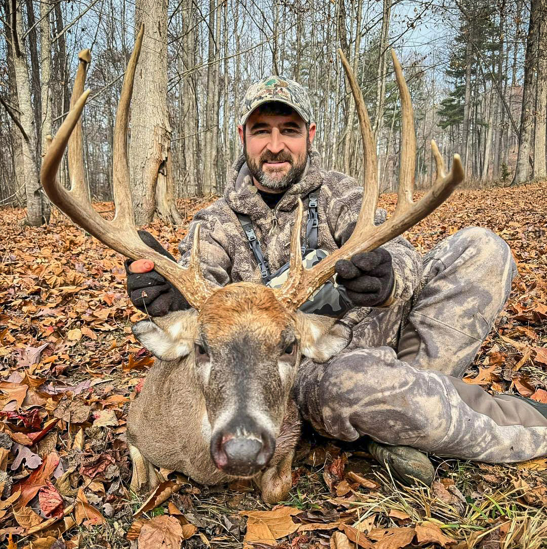 一名身着迷彩服的男子和一只大白尾鹿的照片。