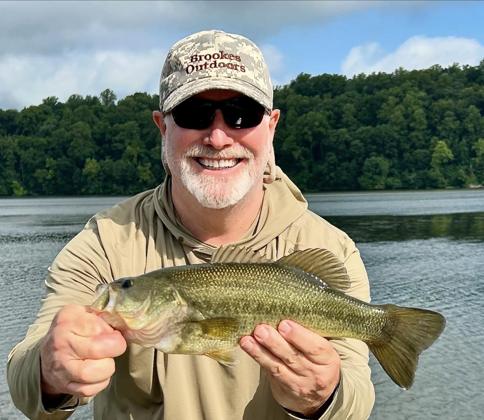 一名男子在河前举着一条大嘴鲈鱼。