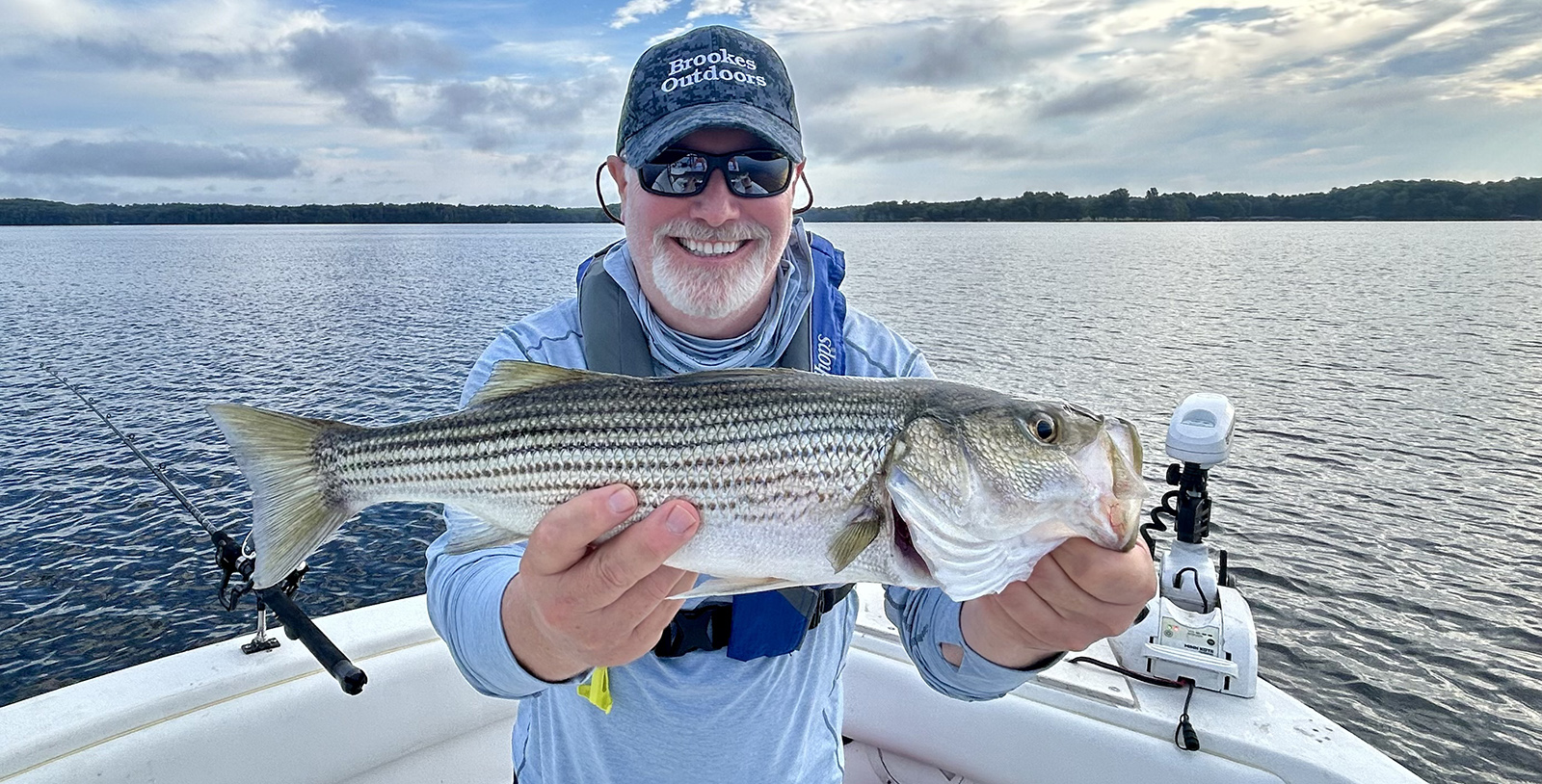一名男子坐在船上，手里拿着一条大鲈鱼，面带微笑。