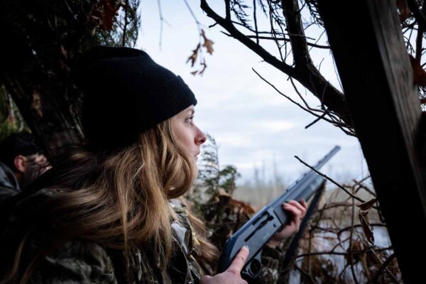 一名身穿迷彩服的女子在水边的狩猎掩体中