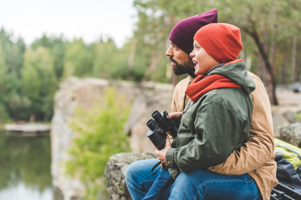 图像中，一名男子抱着一名孩子，孩子拿着双筒望远镜，两人都向左看。